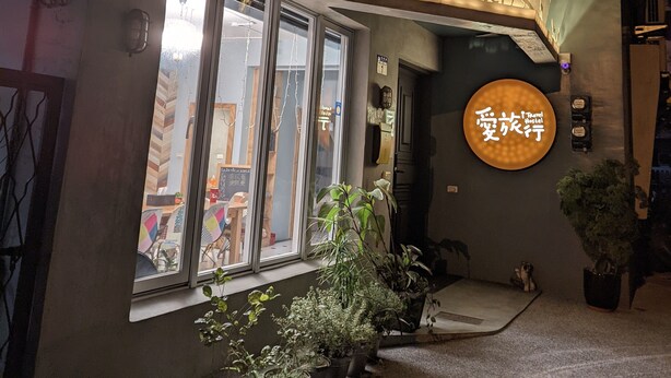 A hostel with a sign reading "Travel Hostel" and a circular sign with Chinese characters. There are potted plants in front of the entrance. - itravel Hostel (Hualien City)