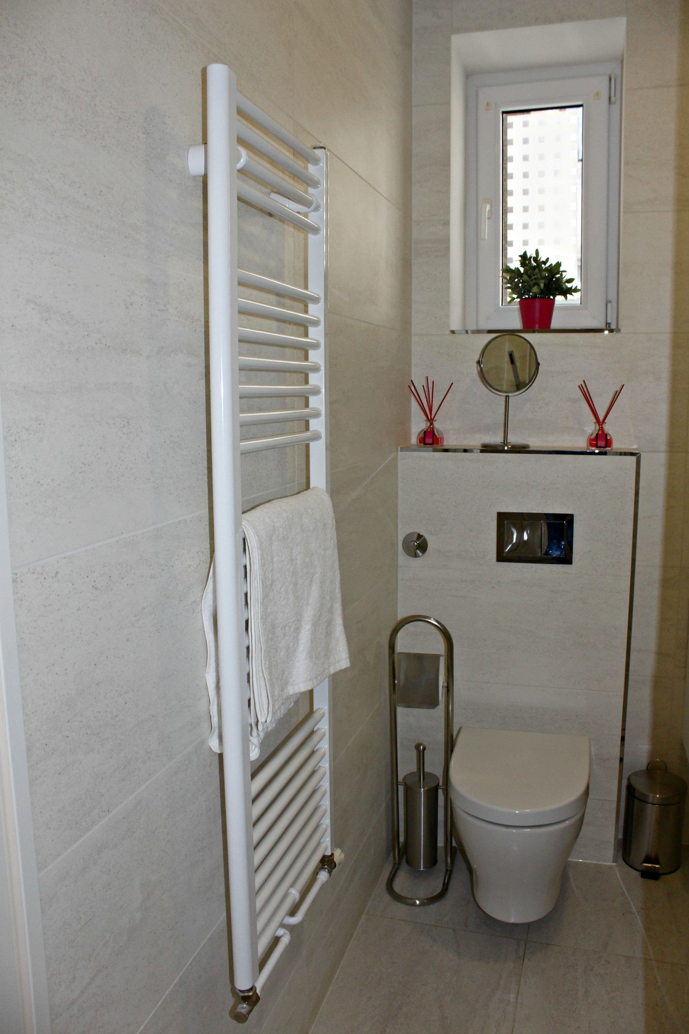A bathroom with a white toilet, a towel rack, a window with a plant, and a mirror.