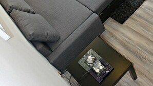 A modern room with a grey sofa, orange cushions, a small table with a decorative item, and a white entertainment unit with a flat-screen TV. - Baltazar Studio Apartment (Zagreb)