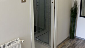 A hallway with a white radiator, a glass door leading to a shower area, and a potted plant. - Baltazar Studio Apartment (Zagreb)
