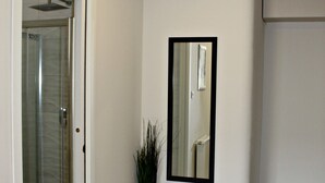 A hallway with a glass shower door, a tall plant, and a mirror on the wall. - Baltazar Studio Apartment (Zagreb)