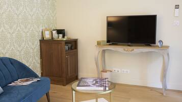 A living room with a blue sofa, a glass coffee table, a television on a white console table, and a wooden cabinet.