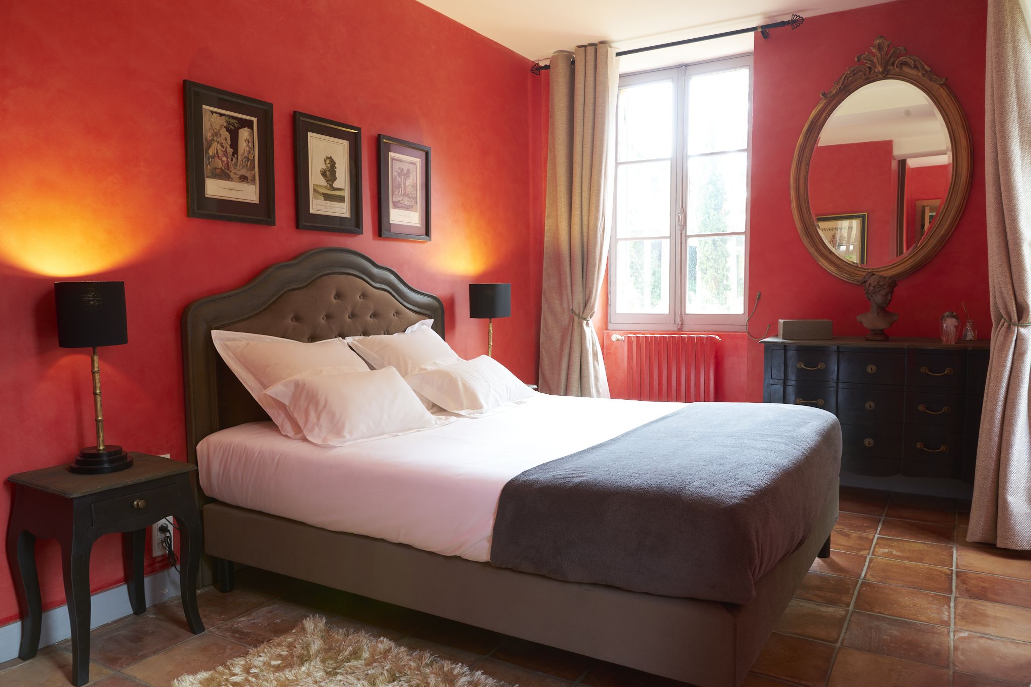 A bedroom with a large bed, two bedside tables with lamps, a dresser, and a mirror on the wall.