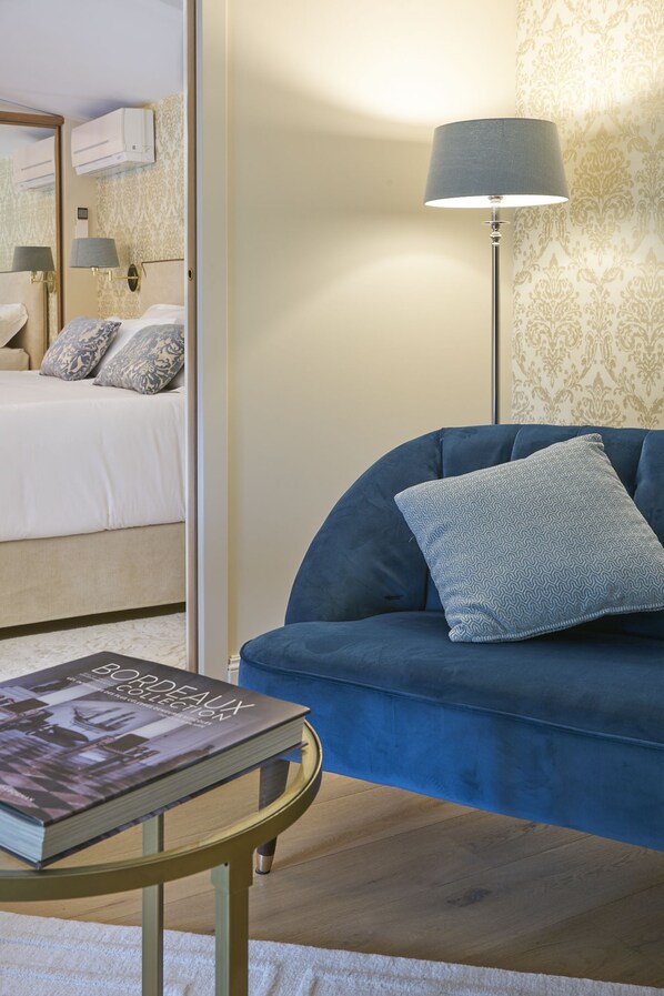 A room with a bed, a blue sofa, a lamp, and a book on a side table. - Château Pont Saint-Martin (Leognan)
