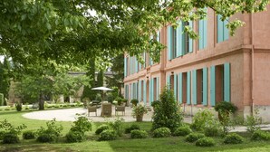 A building with a garden courtyard, outdoor seating, and a large tree providing shade. - Château Pont Saint-Martin (Leognan)