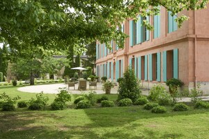 Un edificio con un patio interior con jardín, mobiliario exterior y un gran árbol que da sombra.