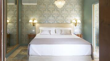 Una cama grande con una colcha blanca y dos mesitas de noche con lámparas, un candelabro y un espejo en la pared.