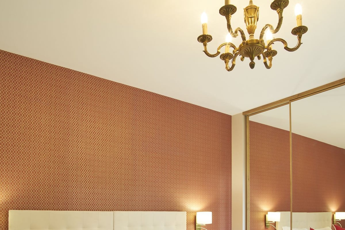 A hotel room with a large bed, a chandelier, a mirror, and a textured wall.