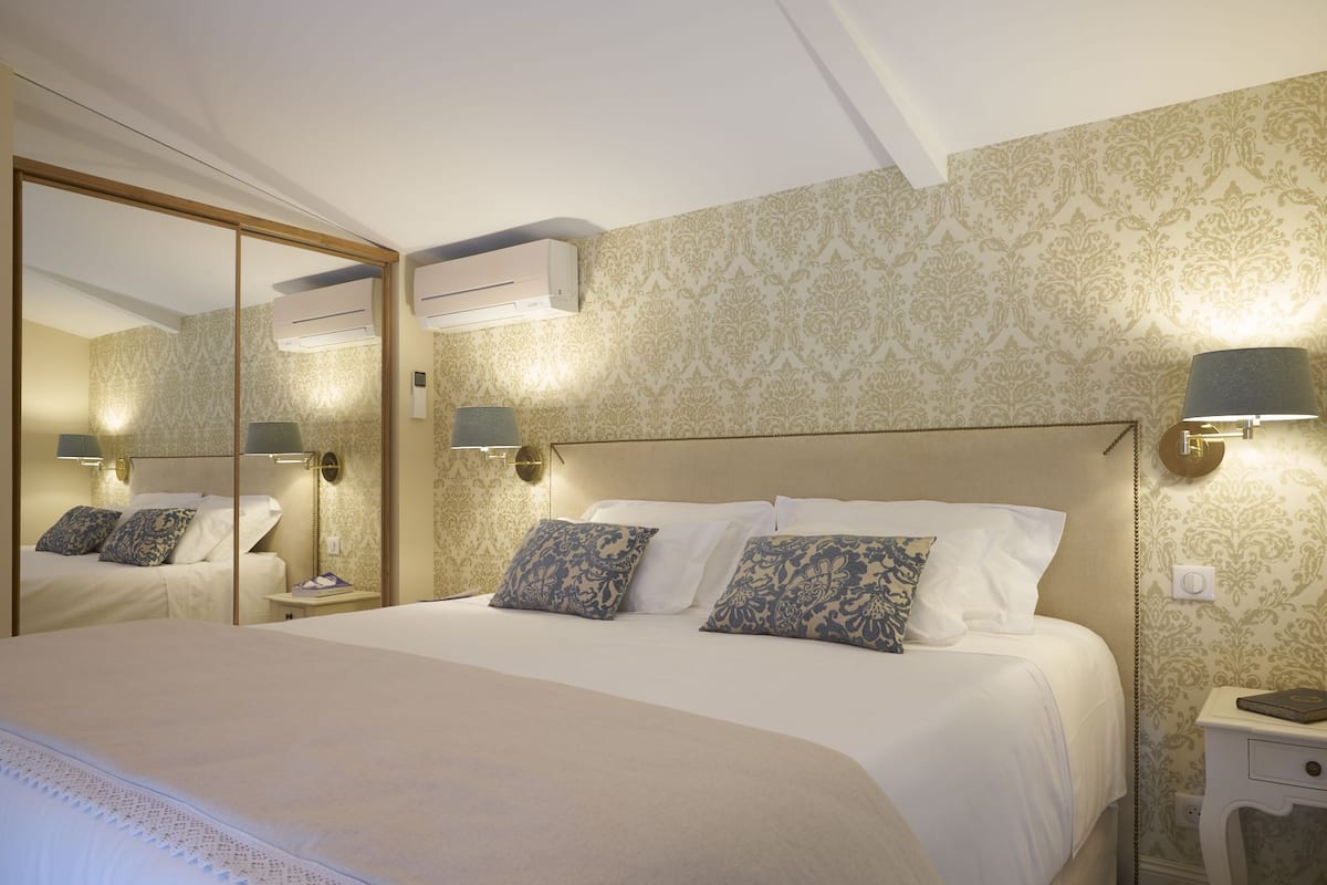 A hotel room with a large bed, a bedside table, a nightstand, a mirror, and wall-mounted lamps.
