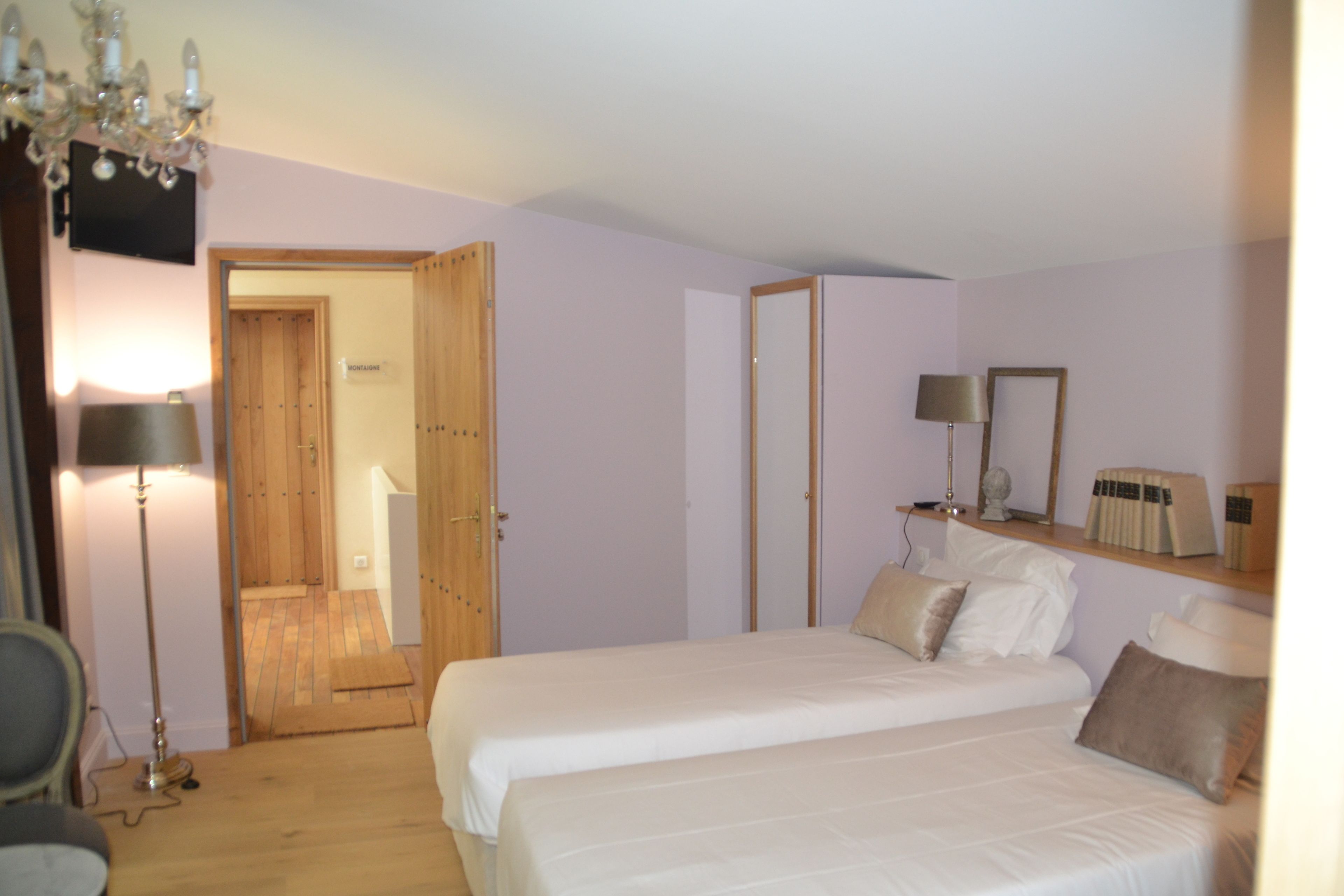 A bedroom with two beds, a wooden door, a mirror, and a chandelier.