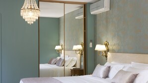 A hotel room with a large bed, a chandelier, a mirror, and wall-mounted lamps. - Château Pont Saint-Martin (Leognan)