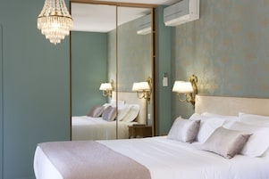 Habitación de hotel con una cama grande, una araña, un espejo y lámparas fijadas a la pared.
