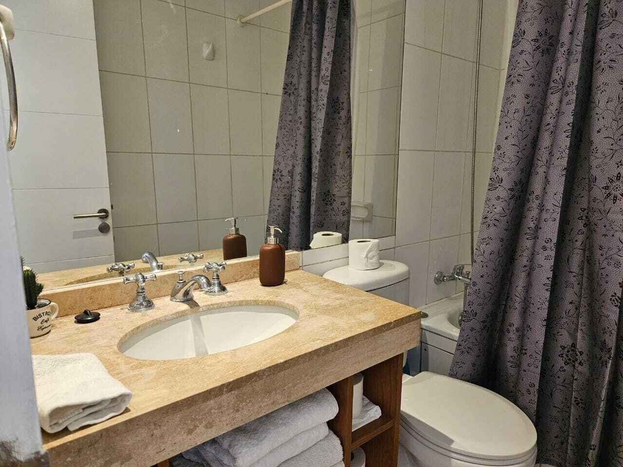 Un baño con lavamanos, espejo, inodoro y cortina de ducha.