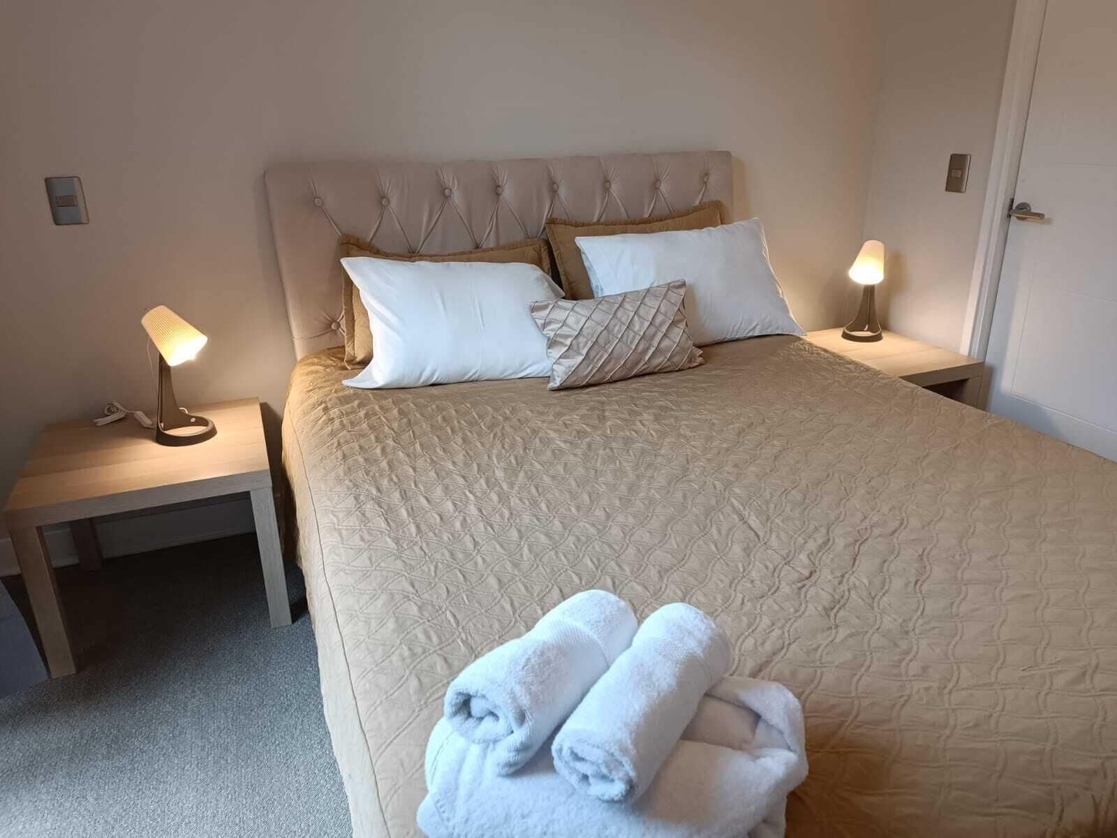 Ein ordentlich bezogenes Bett mit einer gesteppten Decke, zwei Nachttischlampen und ein Paar gefaltete Handtücher auf dem Boden.