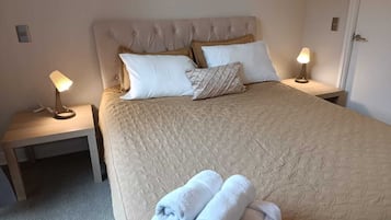 Ein ordentlich bezogenes Bett mit einer gesteppten Decke, zwei Nachttischlampen und ein Paar gefaltete Handtücher auf dem Boden.