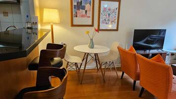 Una sala de estar moderna con zona de cocina, una mesa redonda de comedor con sillas, un sofá y un televisor.