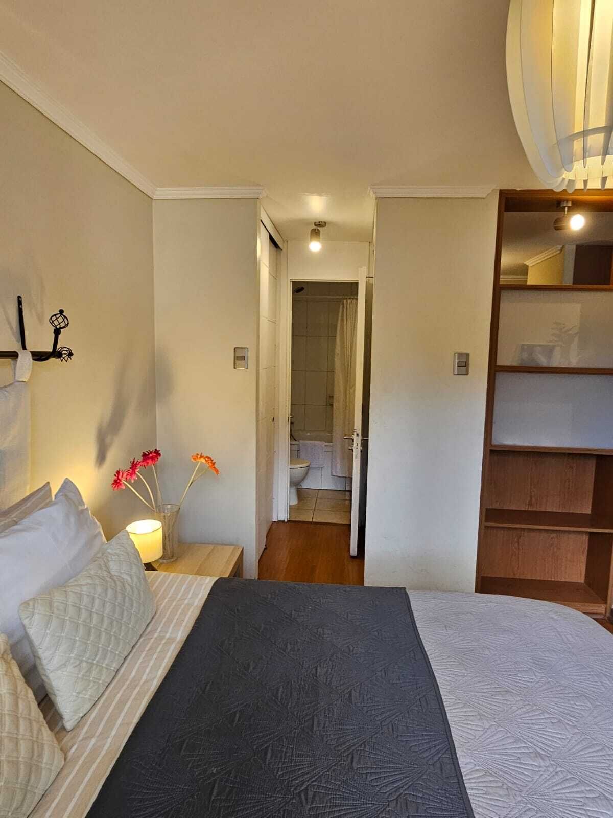 Une chambre à coucher comprenant un lit, des tables de chevet, une commode, un miroir, une armoire et une salle de bain visible à travers une porte ouverte.