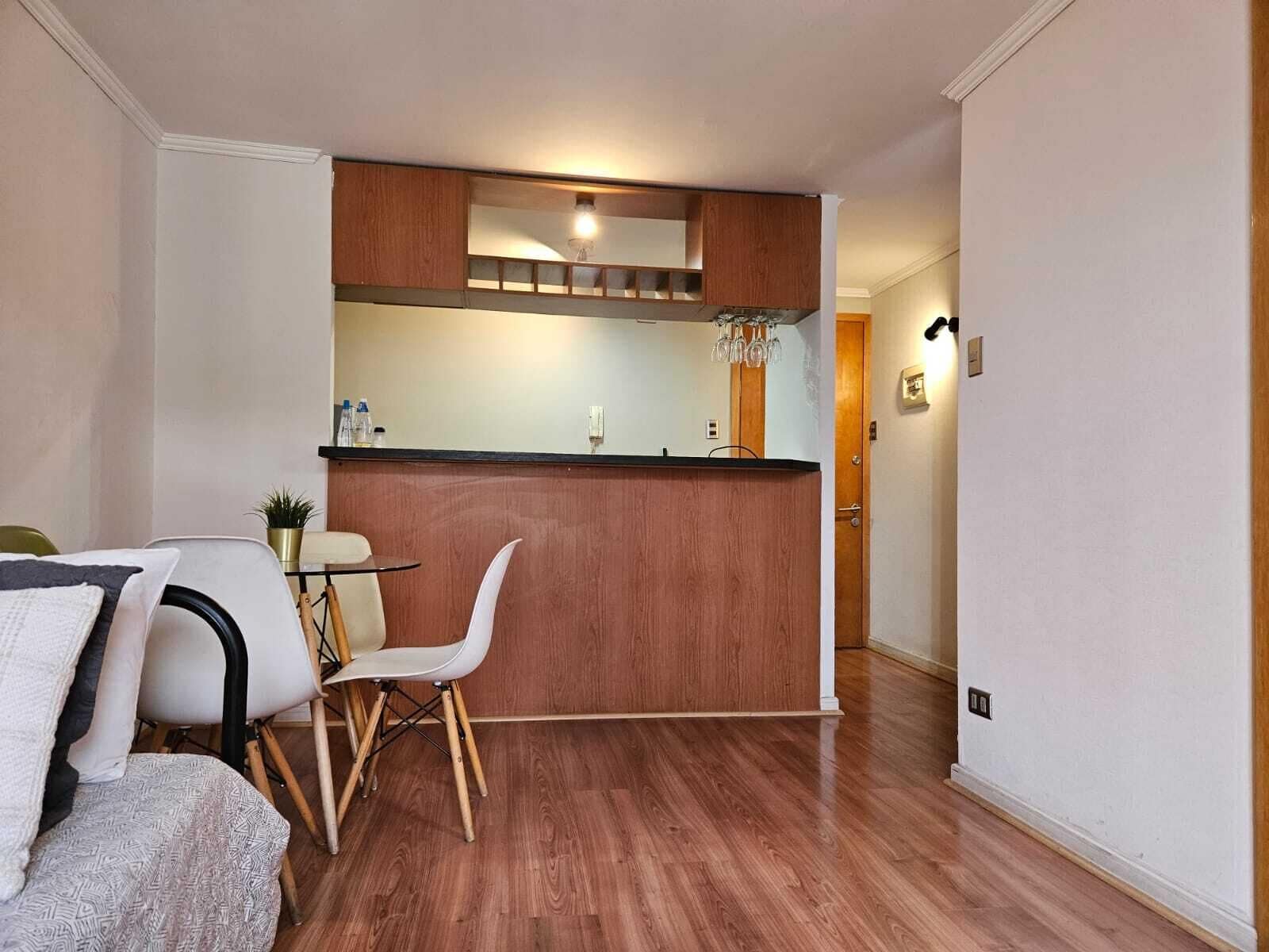 Una cocina compacta con encimera de madera, un rincón comedor con una silla blanca y una mesa pequeña.