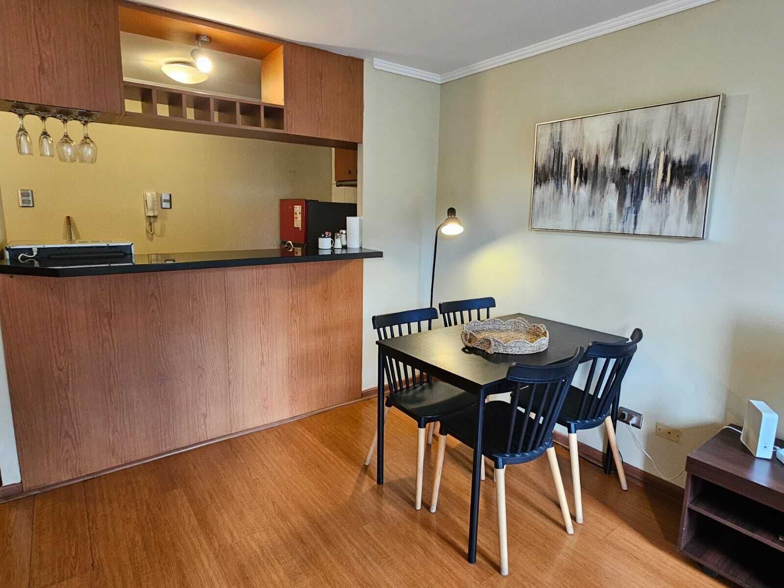 Une cuisine compacte avec un plan de travail en bois, une table à manger avec des chaises, une machine à café et un tableau accroché au mur.