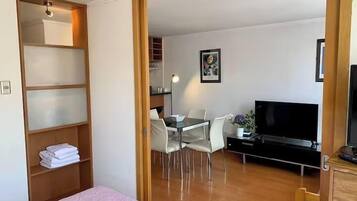 A hotel room with a bed, a desk with chairs, a television, and a wooden wardrobe.