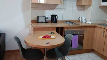 A compact kitchen with wooden cabinets, a round dining table with chairs, a built-in oven, and a microwave.