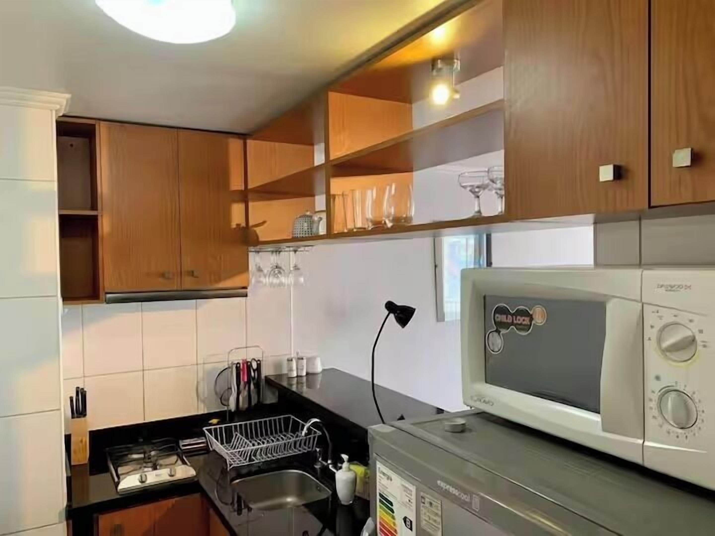 A compact kitchen with wooden cabinets, a microwave, a sink, and a dish rack.