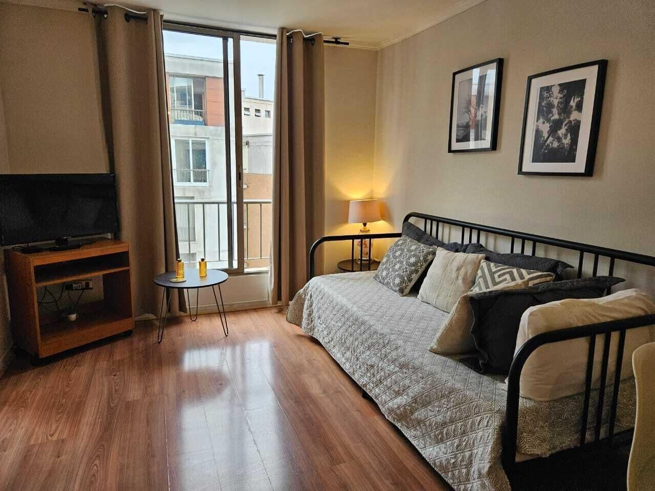 Une chambre d’hôtel avec un lit, une télévision, une petite table, une lampe et une fenêtre avec des rideaux.