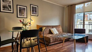 Een moderne woonkamer met een glazen salontafel, een bank, een eettafel met stoelen, en ingekaderde foto's aan de muur.