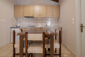 A kitchen with wooden cabinets, a tiled backsplash, a white countertop, and a dining table with chairs. - Plaka Sungrace Studios & Apartments (Zakynthos)