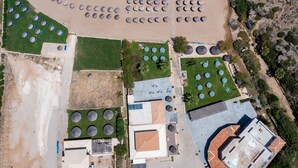 Vue aérienne d’une propriété située sur la côte, avec une plage, plusieurs structures circulaires probablement destinées aux sports nautiques, et un bâtiment doté d’un toit en tuiles.