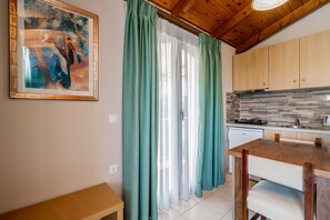 A kitchen with wooden cabinets, a countertop, and a window with green curtains. - Plaka Sungrace Studios & Apartments (Zakynthos)