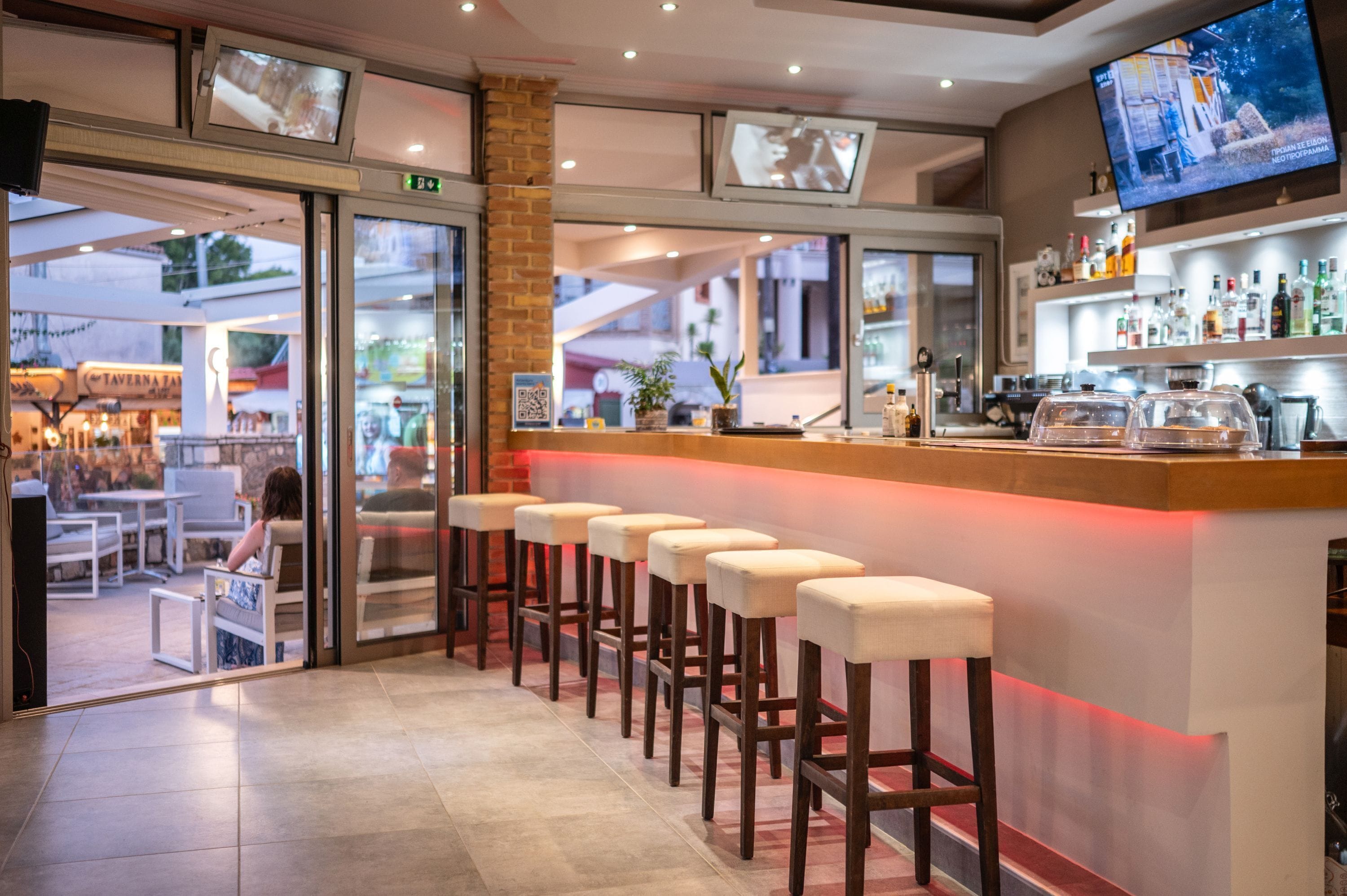 A bar area with a long counter, multiple stools, and a television screen above.