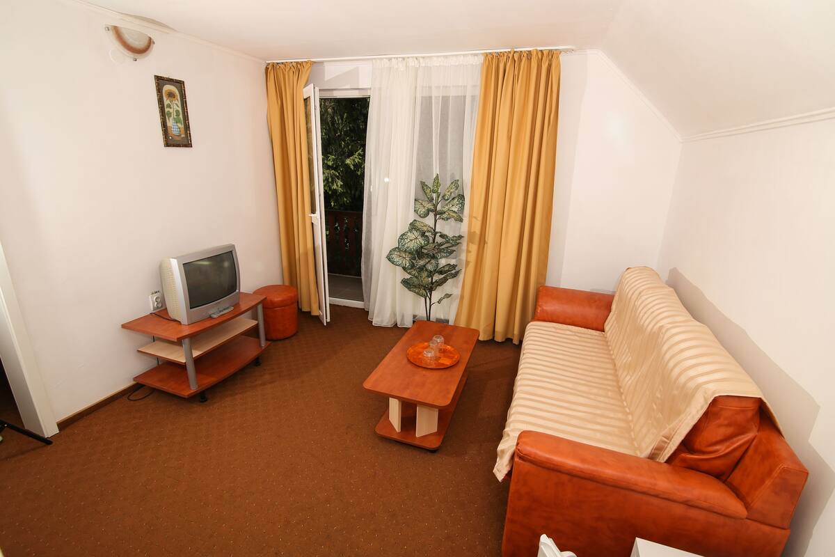 A living room with a sofa, a television on a stand, a small table with a tray, and a sliding glass door with curtains.