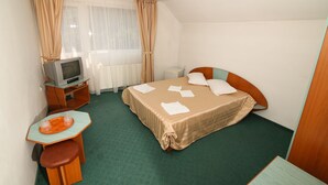Ein kleines Hotelzimmer mit einem Einzelbett, einem Schreibtisch mit Stuhl, einem Fernseher und einem fenster mit Vorhängen.