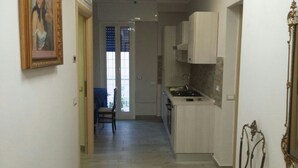 A narrow kitchen with a stove and cabinets, a chair, and a door leading to a balcony. - B&B Fratelli Nicoli (Rome)