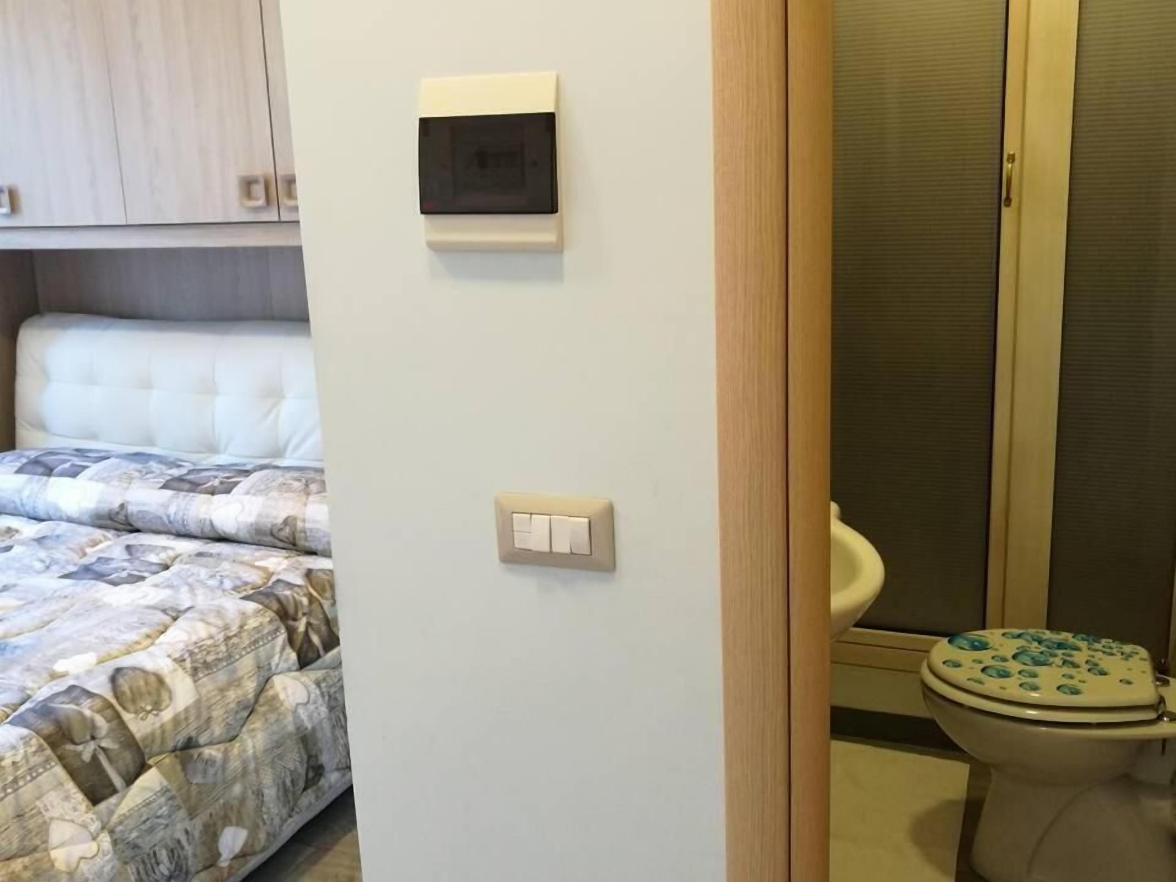 Un dormitorio con cama, un interruptor de luz y un inodoro con asiento azul.