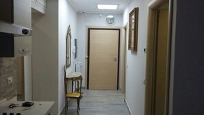 A narrow hallway with a wooden door at the end, a table with a chair, and a mirror on the wall. - B&B Fratelli Nicoli (Rome)