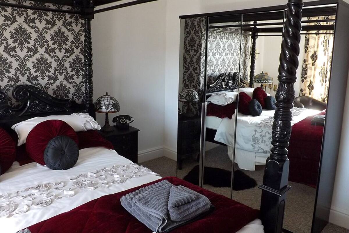 A bedroom with a four-poster bed, a large mirror, and a wardrobe.