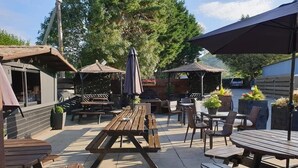 An outdoor patio area with wooden picnic tables and chairs, umbrellas, and potted plants. - Peniarth Arms Hotel (Tywyn)