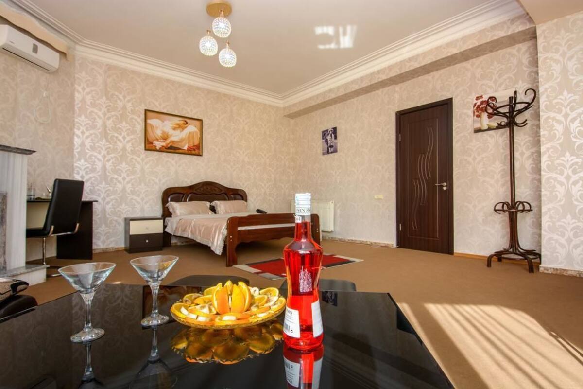 A hotel room with a bed, a desk with a bottle and glasses, a chair, and a decorative wall piece.