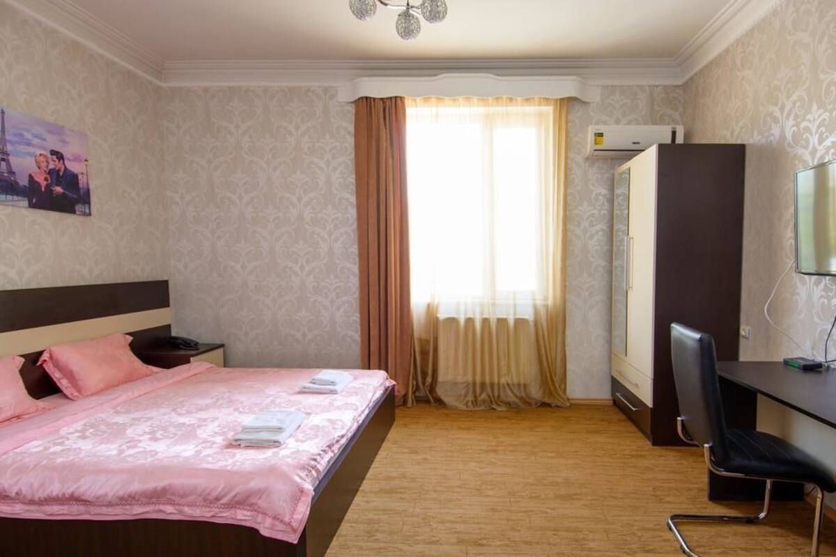 A hotel room with a bed, a desk, a chair, a TV, and an air conditioning unit.