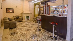 A living room with two sofas, a fireplace, a bar area with shelves of bottles, and a patterned floor.