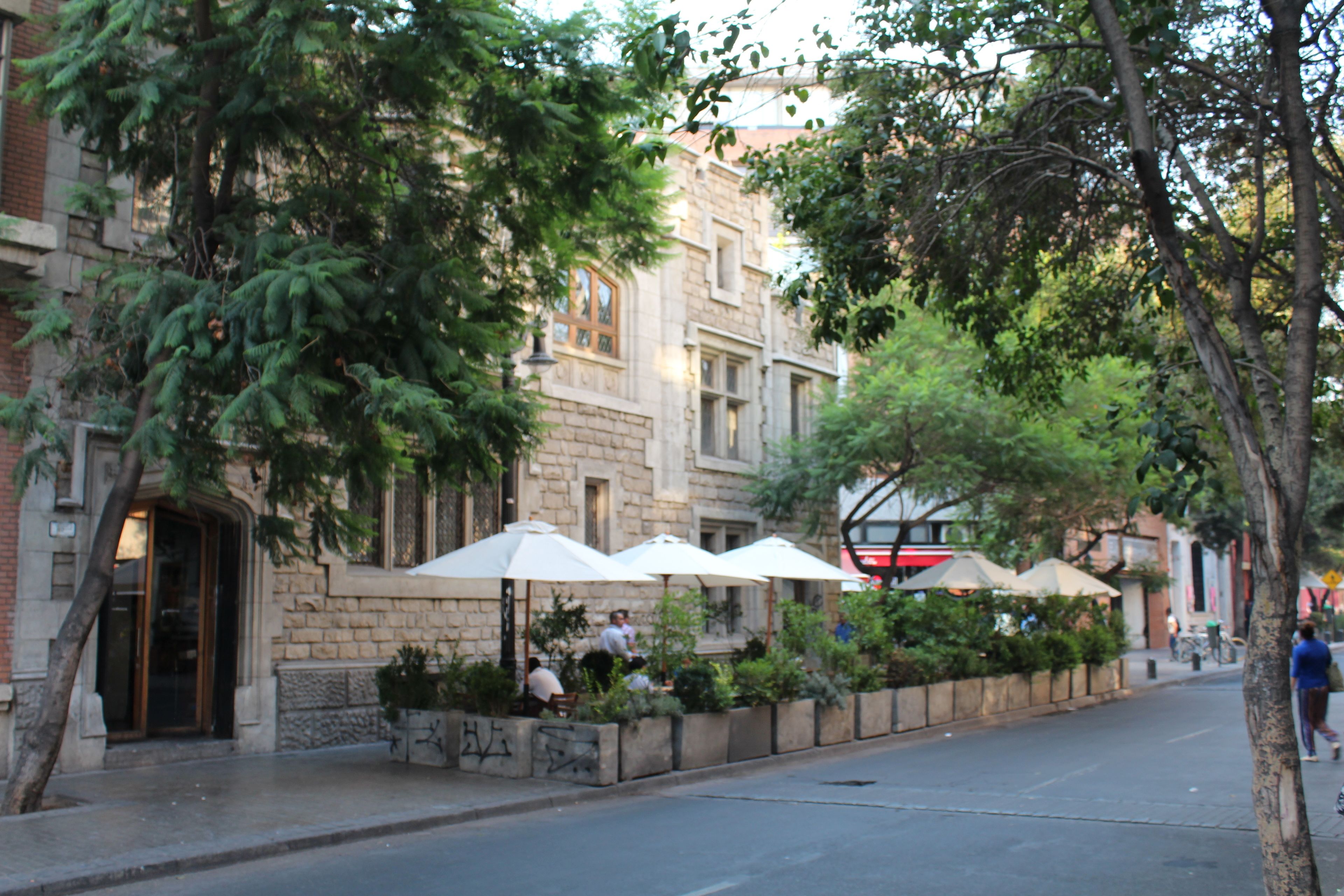 Una calle con terrazas al aire libre, edificios de piedra y árboles.