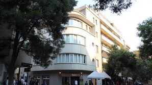 Un immeuble à plusieurs étages doté d’une façade incurvée, d’une entrée au niveau du sol et d’espaces extérieurs aménagés pour s’asseoir.