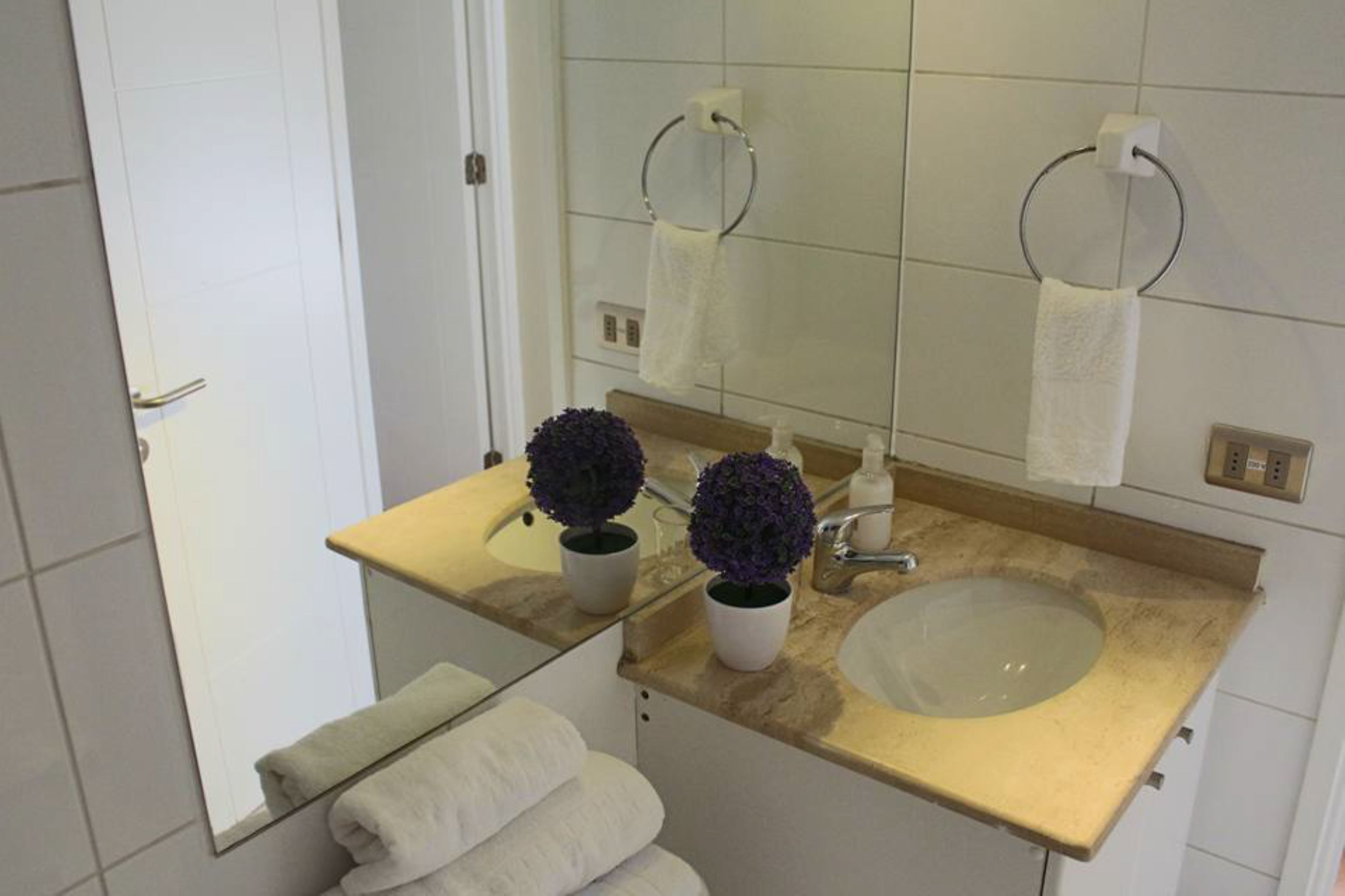 A bathroom with a sink, mirror, two potted plants, and towels.