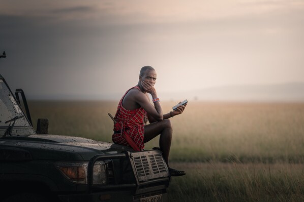A person sitting on the hood of a vehicle in a field.