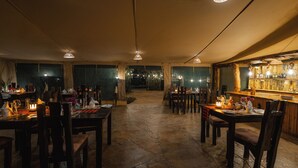 Un comedor amplio con suelo de piedra, mesas y sillas de madera, e iluminación colgante.