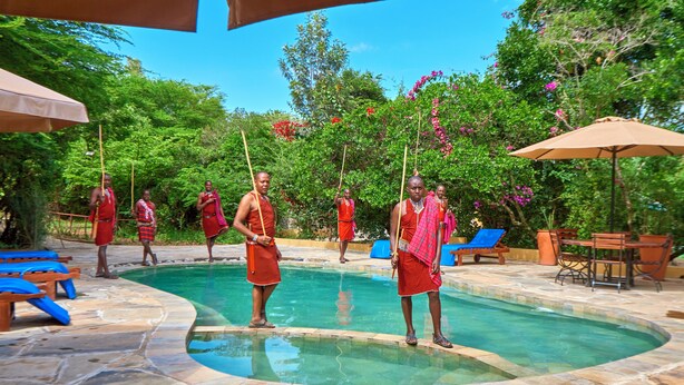 Un área de piscina con suelo de piedra, sillones de descanso y sombrillas.