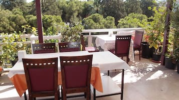 Eine Terrasse im Freien mit Tischen und Stühlen, umgeben von Kübelpflanzen und Bäumen.