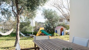 Taula de fusta amb una planta en test, una cadira d'hamaca i un parc infantil amb tobogan.